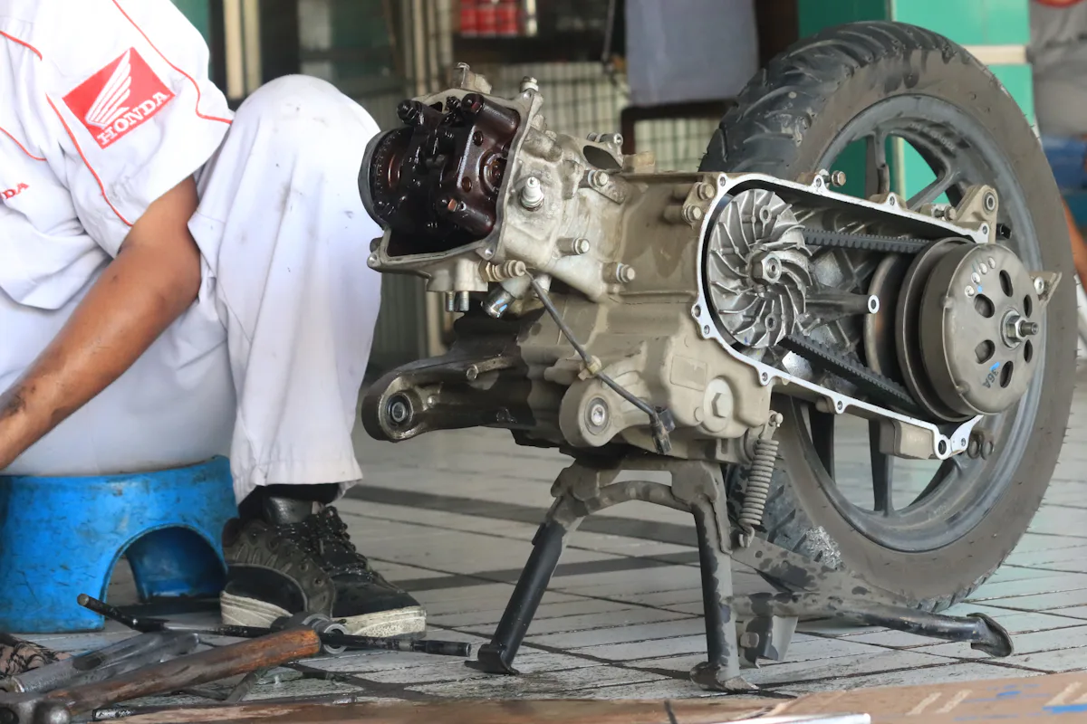 Người thợ thao tác với cụm động cơ và bánh sau xe tay ga tại xưởng