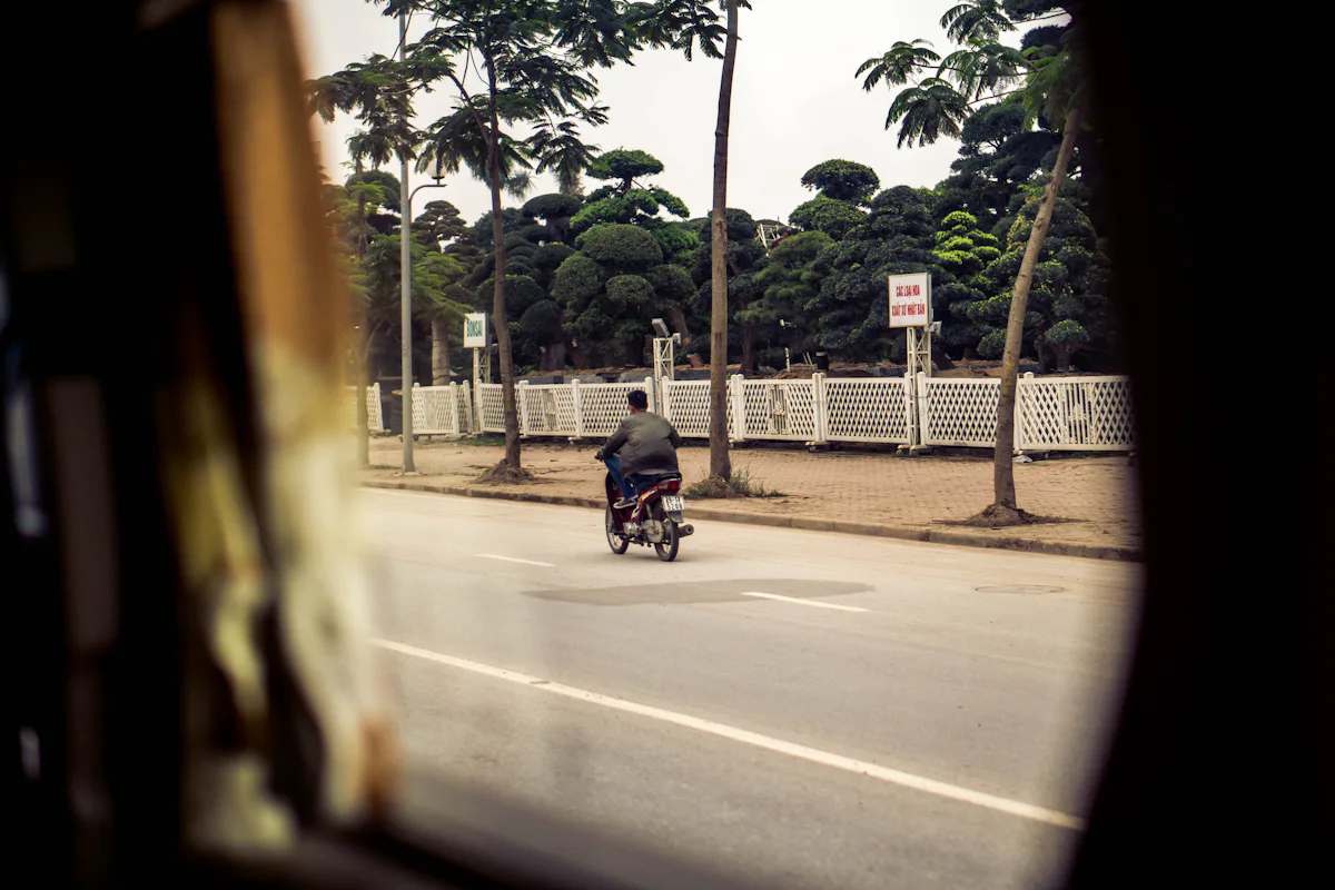 Người đi xe máy trên tuyến đường có hàng cây và hàng rào ven đường