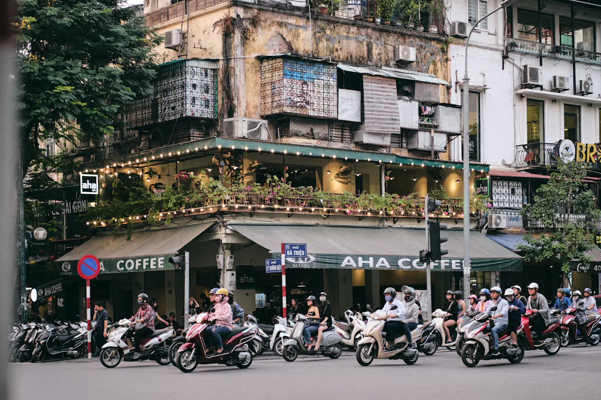 Người đội mũ bảo hiểm đi xe máy qua dãy nhà và quán cà phê trong phố