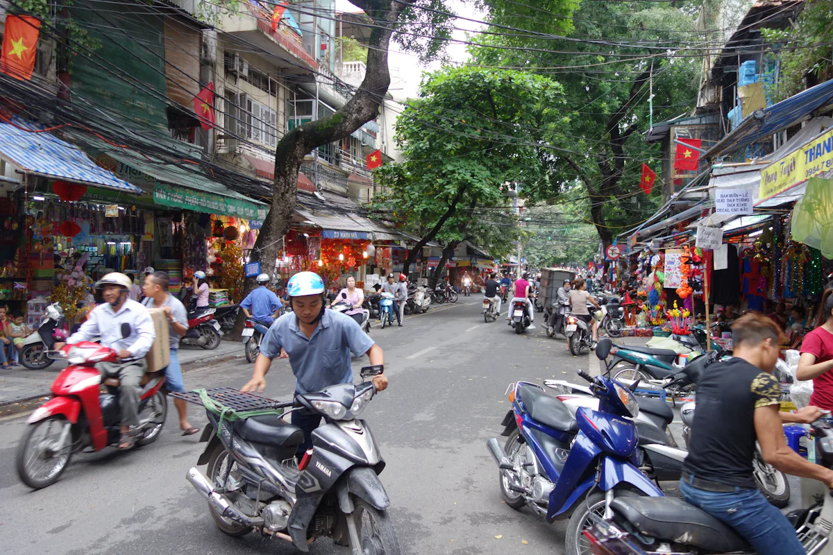 Người đi xe máy qua khu phố có cửa hàng và các xe đỗ bên đường
